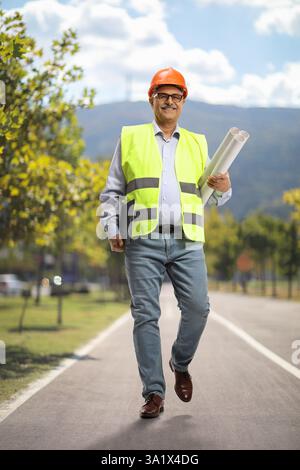 Male engineer holding blueprints and walking in a park Stock Photo