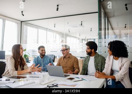 A diverse team of professionals engaged in an active discussion during a business meeting. They brainstorm ideas, analyze data, and collaborate on company growth strategies in a modern office. Stock Photo