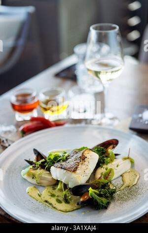 Cod fillet with cauliflower cream, asparagus, clam-wine sauce and mussles. Delicious seafood fish closeup served on a table for lunch in modern Stock Photo