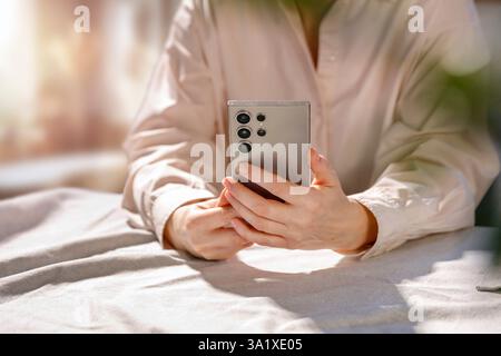 Woman in pink peach shirt sitting at table with hands on the table, holding mobile phone. Copy space for text and product. Stock Photo