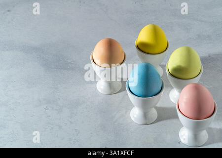 pastel colored easter egg assortment in white cups in diagonal direction on the right on a white marble background. high angle view, Copy space. Stock Photo