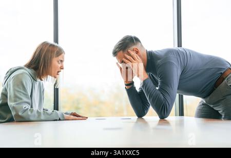 Couple are having quarrel. Woman is sitting by the table, man is standing. Stock Photo