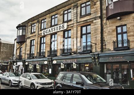 Stone building with "Quayside" signage over storefronts and above windows on upper floors. Cars parked in the street in Whitby, UK. Stock Photo