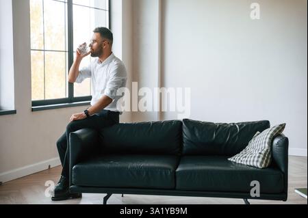 Elegant man in business clothes is indoors with glass of water. Stock Photo