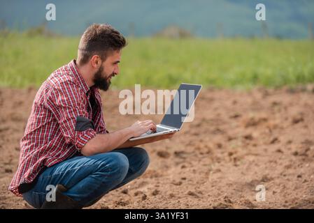 Male farmer plantation checking quality by tablet agriculture modern technology concept smart farming agronomist checking soil quality on the field. Stock Photo