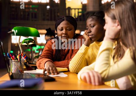 Female teacher assisting pupils with class homework and mentoring them, providing academic instruction and support to help them pass their school assignments. Tutor lecturer gives private lessons. Stock Photo