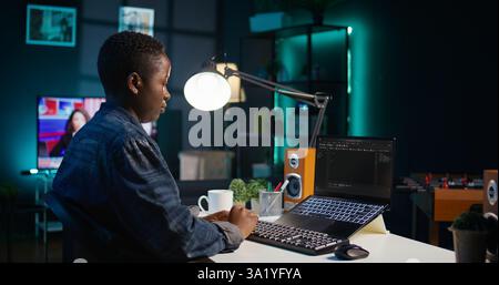 Software developer writes code on laptop screen while in apartment office using Java programming languages. Programmer remotely working on fixing database errors while working from home, camera B Stock Photo