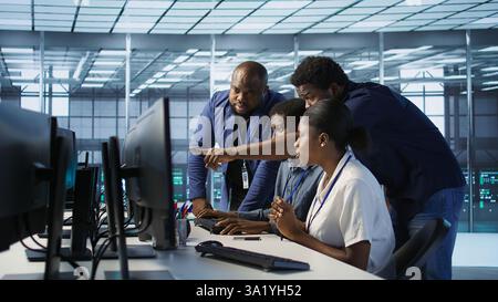 Teamworking engineers talking in server room, developing disaster recovery plans ensuring minimal downtime. Team of data center employees doing brainstorming, monitoring performance, camera A Stock Photo