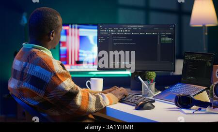 Programmer in home office concentrating on finding bugs while he codes on his computer. African american IT admin frowning while looking at screen, confused by errors in lines of code. Camera A. Stock Photo