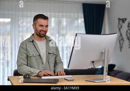A happy man using a desktop computer while working at a home. Stock Photo