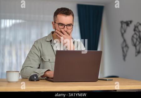 A worried man using a laptop while working at home office. Stock Photo
