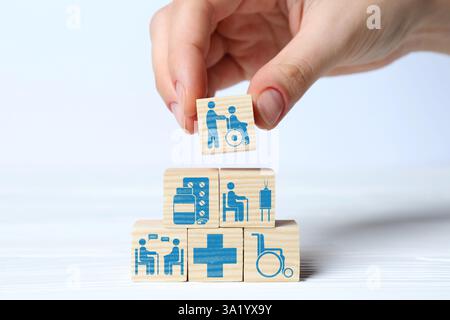 Woman building pyramid of cubes with healthcare icons on white background, closeup Stock Photo