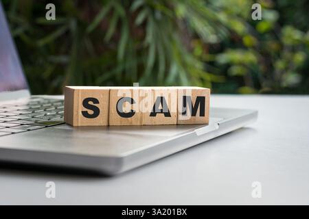 SCAM word on wooden blocks on top of computer laptop. Stock Photo