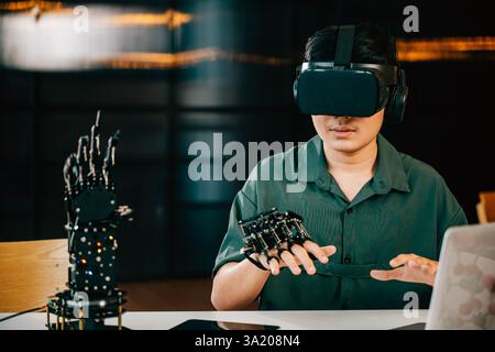 Asian teenager experiments with a robot arm project using VR glasses in a classroom. Embracing Stock Photo