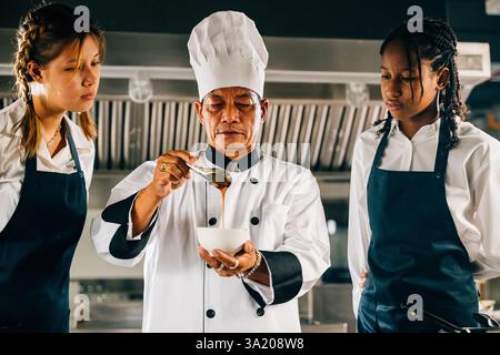 Professional Asian senior chef instructs diverse students in a restaurant kitchen focusing on Stock Photo