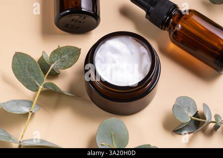 brown glass cream jar on beige background with eucalyptus branch. Skin care cosmetic concept Stock Photo