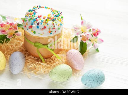 Easter cake decorated with colorful sprinkles and tied with green ribbon surrounded by pastel colored eggs and flowers Stock Photo