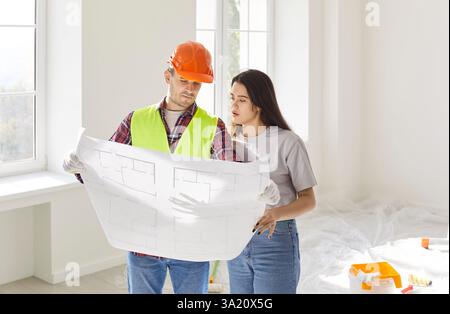 Foreman worker and female client watching flat plan to supervise, direct, worker looking at project Stock Photo
