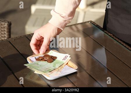 Waitress taking payment for order from wooden table at outdoor cafe, closeup. Leave tip Stock Photo