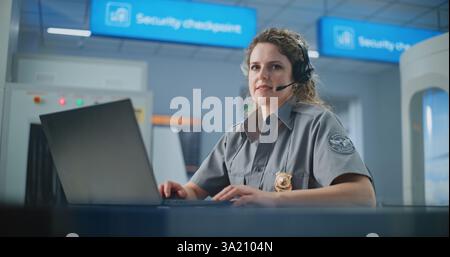 Airport Security Checkpoint: Female Security Officer in Headset Using Laptop, Looking at Camera. Transportation Security Administration for Travel Safety. In the Background, Airport Staff Working. Stock Photo