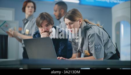 Airport Security Checkpoint: Two Diverse TSA Workers Using Laptop, Discussing Security Issues. Transportation Security Administration for Travel Safety. In the Background, Airport Staff Working. Stock Photo