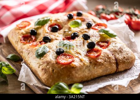 Focaccia - Italian Bread with tomatoes basil leaves olives and olive oil on cutting board. Stock Photo
