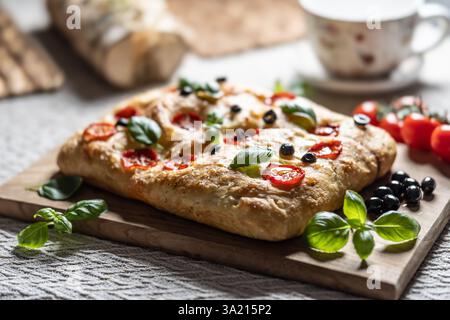 Focaccia - Italian Bread with tomatoes basil leaves olives and olive oil on cutting board. Stock Photo