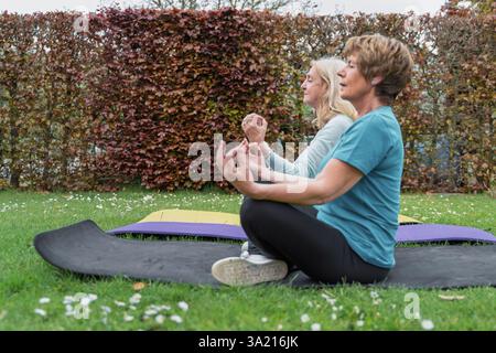Two senior women meditating outdoors on grass, practicing mindfulness and yoga for mental health, relaxation, and healthy aging in a natural environme Stock Photo