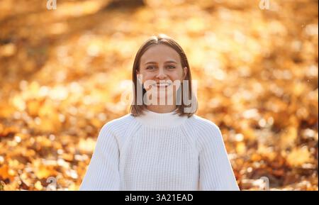 Portrait of cheerful young woman in white shirt and in autumn forest that is smiling. Stock Photo