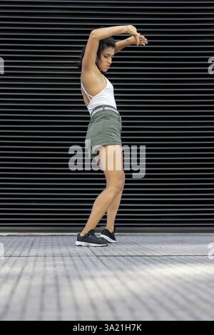 Confident young woman dancing against a modern backdrop in the street Stock Photo