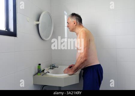 Man 60 plus looks at himself in the bathroom mirror Stock Photo