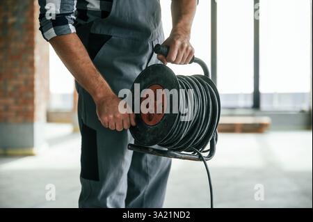 Holding wires. Close up view of repairman indoors in unfinished building. Stock Photo