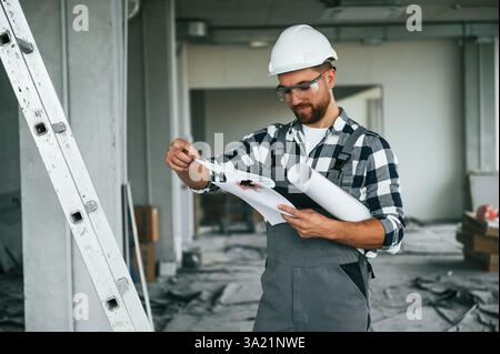 Manager is with plan in hands. Repairman in uniform is in the unfinished building. Stock Photo