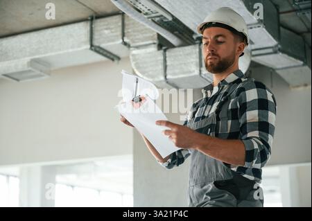 Checking the ceiling. Construction worker in uniform in empty unfinished room. Stock Photo
