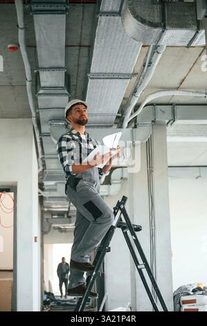 Checking the ceiling. Construction worker in uniform in empty unfinished room. Stock Photo