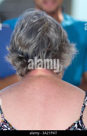 Short-haired woman seen from behind, wearing a vibrant outfit, captured candidly in a serene outdoor setting with a calm and reflective mood. Stock Photo