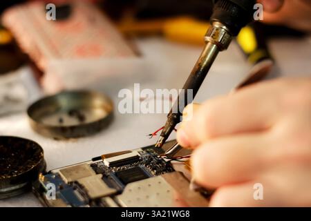 A close-up of a technician using a soldering iron to repair a phone, with a blurred background highlighting precision work in electronics. phone repai Stock Photo