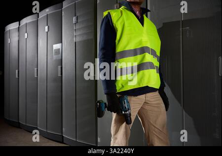 Maintenance worker holding cordless drill, standing in server room. Stock Photo