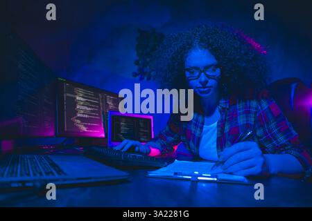 Young female programmer working on code in a modern workspace with multiple monitors, showcasing focus Stock Photo