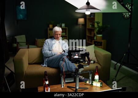 Man working on content creation in cozy home studio featuring modern lighting and recording equipment. Displaying organized background with shelves and artistic elements Stock Photo