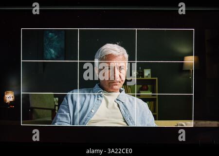 Portrait of elderly man sitting on a couch in a warmly lit living room with lamps in background, calmly looking at camera Stock Photo