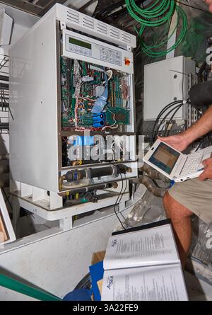 Technician Using Laptop to Diagnose Advanced Equipment in Industrial Environment Stock Photo