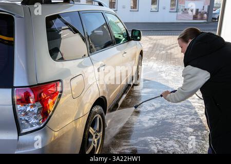 Woman Using High-Pressure Washer to Clean a Dirty SUV at a Self-Service Car Wash Stock Photo