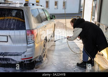 Woman Using High-Pressure Washer to Clean a Dirty SUV at a Self-Service Car Wash Stock Photo