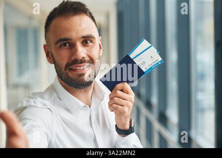 Smiling, holding tickets. Young handsome man in the airport. Stock Photo