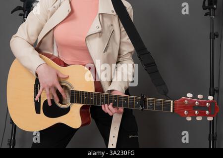 Faceless female guitarist strumming classical six string acoustic guitar. Close-up front view of unrecognizable young woman musician dressed in beige Stock Photo