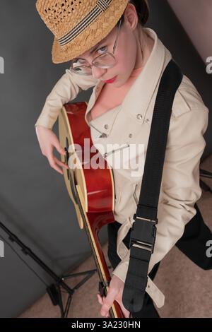 High angle view woman guitarist truly breathtaking and way she's playing acoustic guitar and looking at camera is captivating. Dutch angle dynamic per Stock Photo