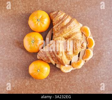 Delicious fresh croissants with vibrant oranges and sliced tangerines on wooden board. Stock Photo