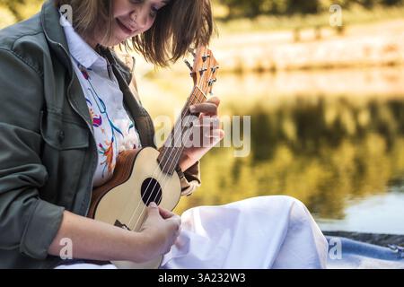 Young woman musician playing ukulele outdoors. Relaxation with acoustic music string instrument Stock Photo