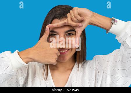 Young woman framing her face with fingers on blue background Stock Photo